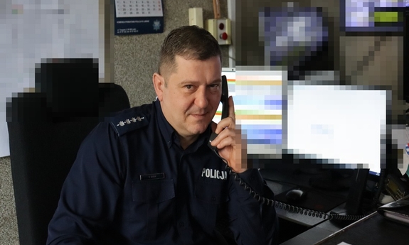 w pomieszczeniu policjant ze słuchawką telefoniczną przy uchu