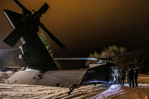 Nocne ujęcie ośnieżonego śmigłowca na górskim lądowisku, obok niego kilku mężczyzn.