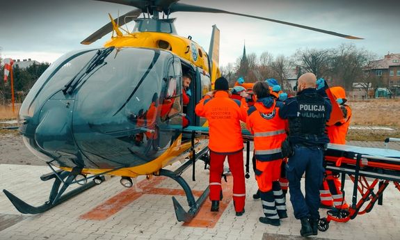 Medycy i policjant transportują poszkodowanego do śmigłowca