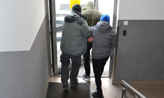 dwóch nieumundurowanych policjantów wyprowadza zatrzymanego z budynku komendy