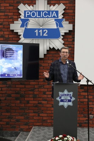 mężczyzna przemawia stojąc przy mównicy, w tle na ścianie gwiazda policyjna