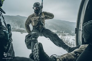 Na tle ośnieżonych gór w otwartych drzwiach lecącego Black Hawka do desantu szykuje się kontrterrorysta.