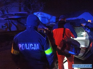 Na zdjęciu policjant i ratownik medyczny stojący koło samochodu