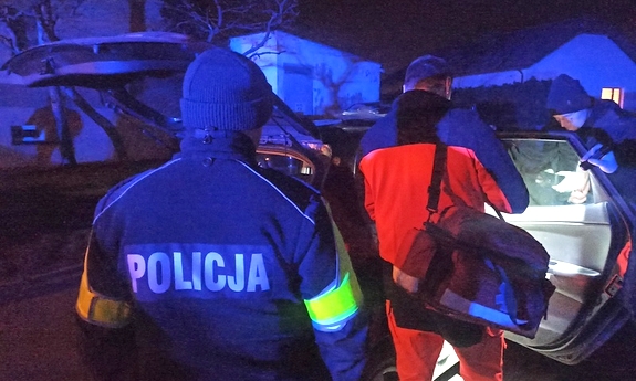 Na zdjęciu policjant i ratownik medyczny stojący koło samochodu