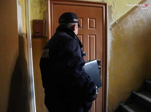 umundurowany policjant stoi przy drzwiach mieszkania na klatce schodowej