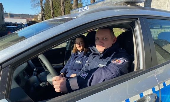 policjant i policjantka w radiowozie - widok z boku przez opuszczona szybę auta
