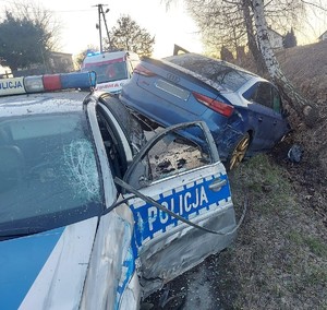 Miejsce zderzenia pojazdów, oznakowanego radiowozu i samochodu marki Audi koloru niebieskiego. W tle karetka