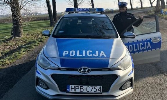 Na dworze na drodze policjantka ruchu drogowego stojąca przy otwartych drzwiach policyjnego radiowozu