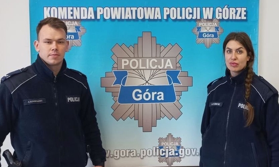 W pomieszczeniu policjanci w mundurach przy plakacie Komendy Powiatowej Policji w Górze