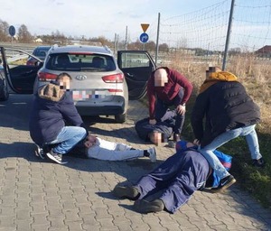 Mężczyźni zatrzymani przez policjantów leżą przy drodze