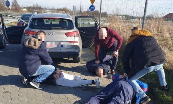 Mężczyźni zatrzymani przez policjantów leżą przy drodze