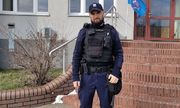 Policjant w umundurowaniu w czapce z daszkiem stoi przed komisariatem