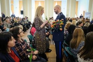 policjant wręcza kwiaty zgromadzonym na auli kobietom