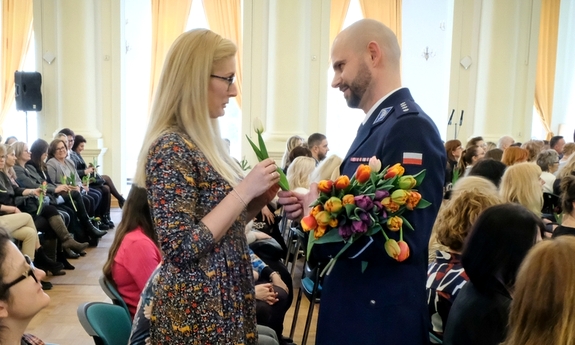 policjant wręcza kwiaty zgromadzonym na auli kobietom