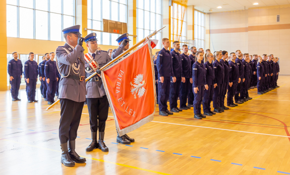 poczet sztandarowy i widoczni stojący na miejscu zbiórki policjanci