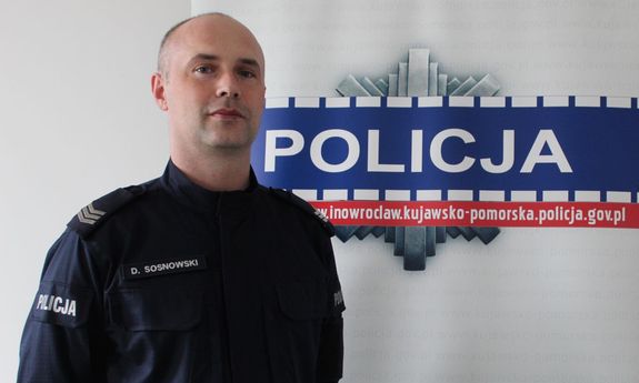 policjant sierż. szt. Dawid Sosnowski stoi na tle policyjnego baneru