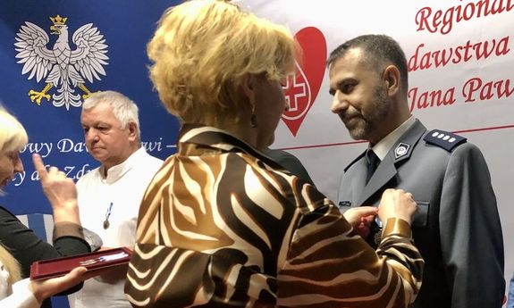 kobieta przypina policjantowi odznaczenie - widok  z boku
