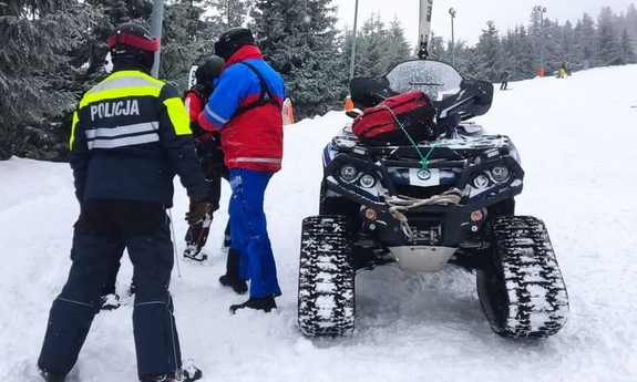 policyjny patrol narciarski pomaga poszkodowanej kobiecie na stoku