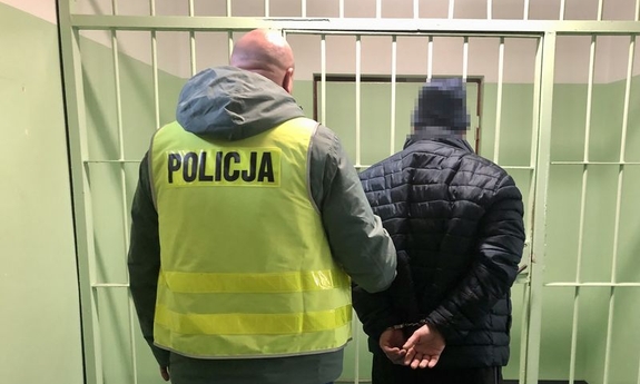 policjant z zatrzymanym w kajdankach, w pomieszczeniu, w tle kraty