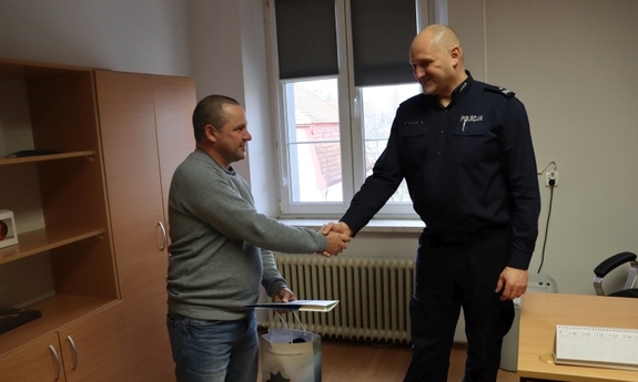 I Zastępca Komendanta Powiatowego Policji w Lubinie p.o. podinsp. Marek Szczepański gratuluje mężczyźnie bohaterskiej postawy, mężczyzna trzyma w ręku list gratulacyjny i upominek
