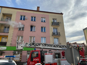 wóz straży pożarnej przed budynkiem, z okna na drugim piętrze wydobywa się dym