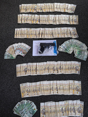 Zdjęcie przedstawia rozłożone na stole pieniądze w różnych nominałach. Pomiędzy nimi leży broń w foliowym opakowaniu.