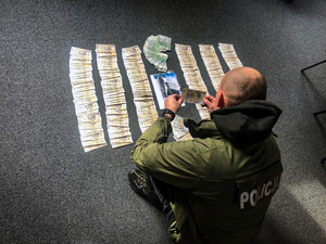 Zdjęcie przedstawia policjanta, który pochyla się nad pieniędzmi rozłożonymi na podłodze.