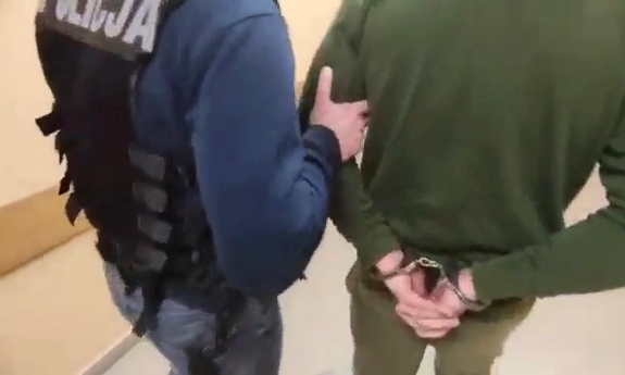 policjant prowadzi zatrzymanego mężczyznę skutego kajdankami