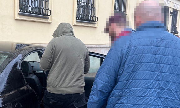 dwaj policjanci z zatrzymanym mężczyzną przy radiowozie
