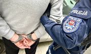 policjant prowadzi zatrzymanego, który ma ręce skute z tyłu kajdankami