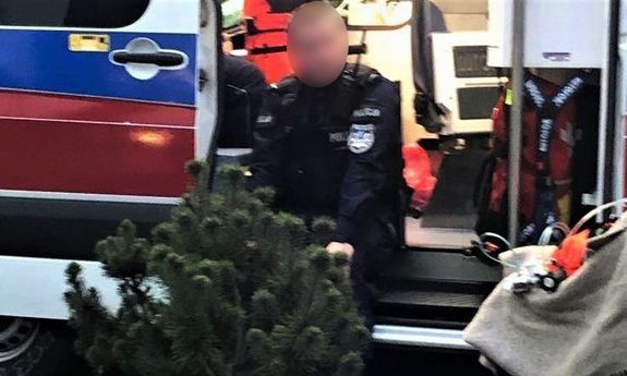 Zdjęcie przedstawia umundurowanego policjanta, który siedzi na progu otwartych drzwi karetki pogotowia.