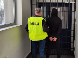 policjant z zatrzymanym mężczyzną zakutym w kajdanki na korytarzu