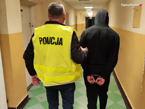 policjant z zatrzymanym mężczyzną zakutym w kajdanki na korytarzu