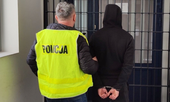 policjant z zatrzymanym mężczyzną zakutym w kajdanki na korytarzu