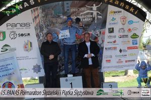 zawodnik stoi na podium trzymając medal i nagrodę