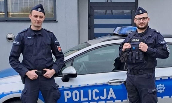 dwaj policjanci stoją przy radiowozie