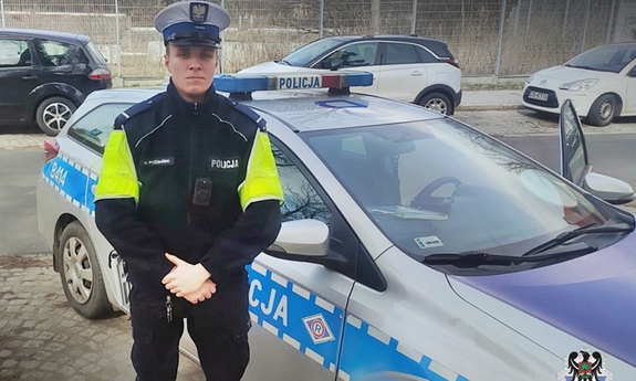 Na zdjęciu jeden z policjantów biorących udział w pilotażu stojący koło radiowozu