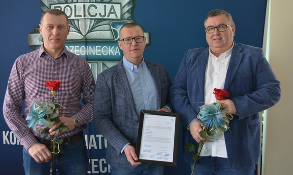 trzej mężczyźni, dwóch z nich trzyma po jednej róży, trzeci trzyma podziękowania oprawione w ramki
