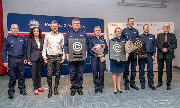 policjanci i policjantki pozują do zdjęcia, dwaj policjanci i policjantka  trzymają w rękach nagrody w formie certyfikatu oprawionego w ramki, jedna policjantka trzyma bukiet kwiatów