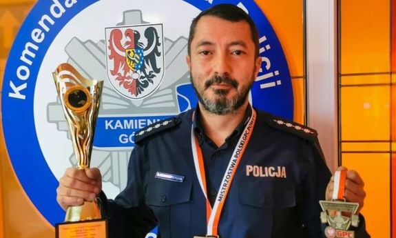 Zdjęcie przedstawia umundurowanego policjanta, który uśmiecha się do zdjęcia trzyma w dłoniach puchar oraz medal.