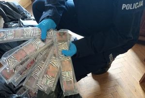 Zdjęcie przedstawia sylwetkę umundurowanego policjanta, który trzyma w dłoniach ubranych w ochronne rękawiczki opakowania z podrobionymi papierosami.