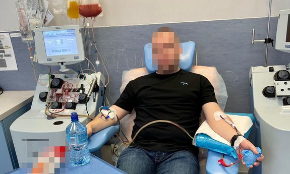 Zdjęcie przedstawia mężczyznę, który siedzi w pokoju medyczny, na fotelu i ma podłączoną kroplówkę do jednej ręki.