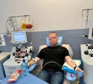 Zdjęcie przedstawia mężczyznę, który siedzi w pokoju medyczny, na fotelu i ma podłączoną kroplówkę do jednej ręki.