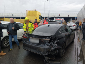 zdjęcie z sytuacji na drodze, uszkodzone samochody, wokół stojące osoby oraz osoba z kamerą