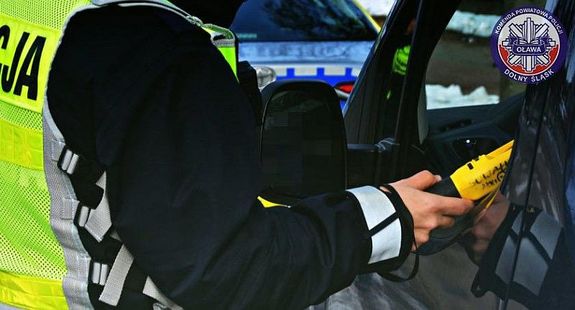 Zdjęcie przestawia fragment sylwetki policjanta, który trzyma w dłoni żółty alkomat bezprzewodowy.