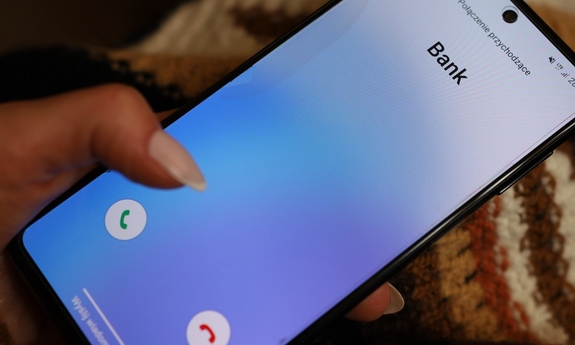Dłoń trzymająca telefon, na ekranie którego wyświetla się nazwa dzwoniącego: bank