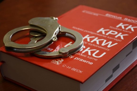 Zdjęcie przedstawia kodeks z czerwoną okładką na której leżą kajdanki w kolorze srebrnym.