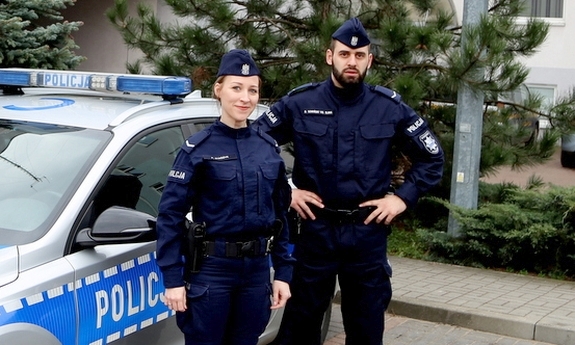 policjant i policjantka stoją przy radiowozie