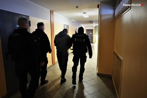 zatrzymany prowadzony przez policjantów na korytarzu w budynku
