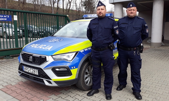 dwaj policjanci stoją przed radiowozem policyjnym